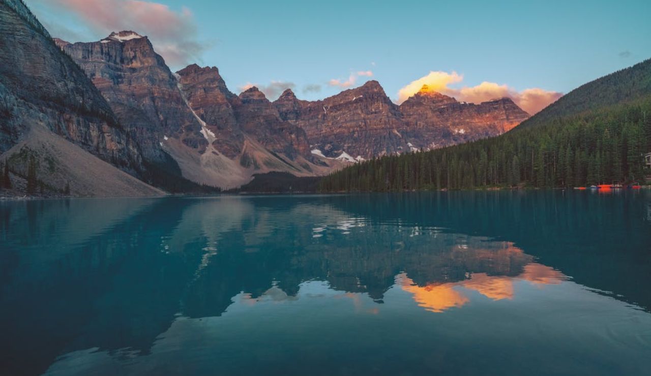 Mountain peaks reflecting on the calm turquoise waters of Moraine Lake at sunset in Banff National Park, Canada.