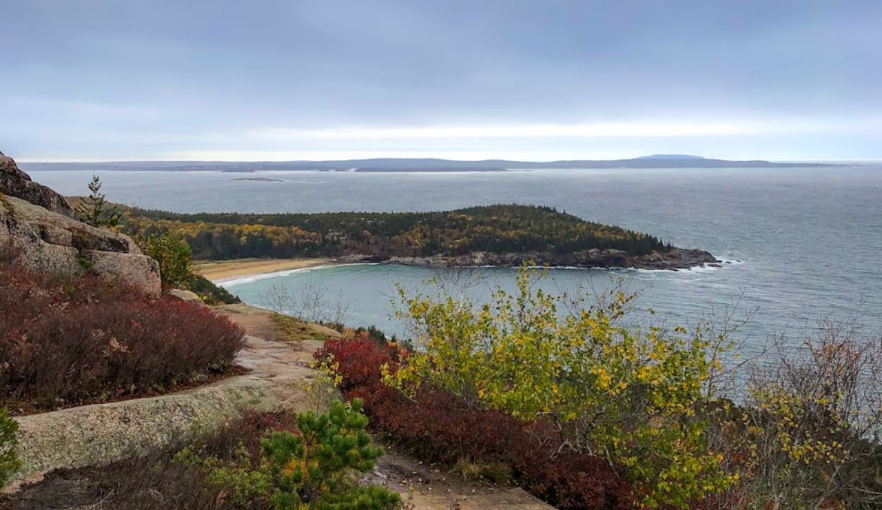 Scenic coastal view of a rocky trail leading to a secluded beach surrounded by forested cliffs.