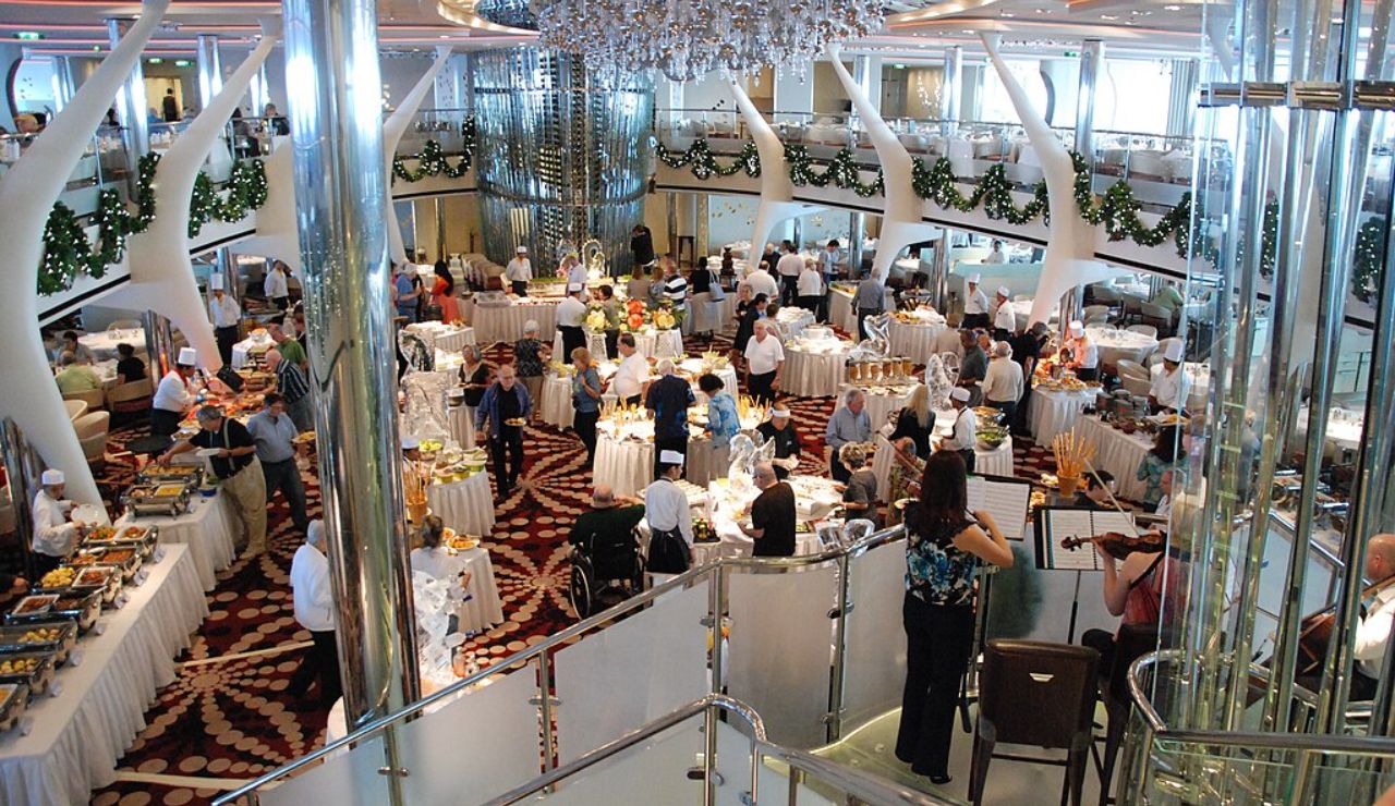 Elegant cruise ship dining hall with buffet tables, guests, and live musicians.