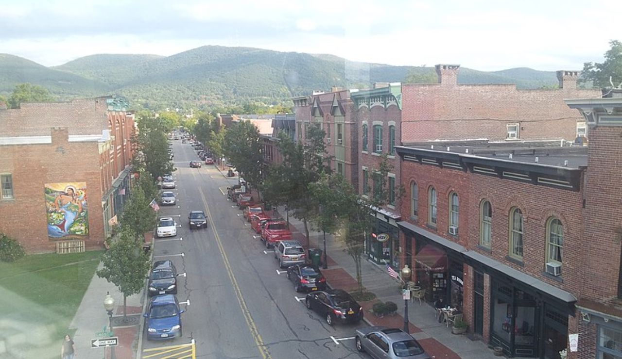 A charming small-town street lined with red-brick buildings and nestled beneath green rolling hills.