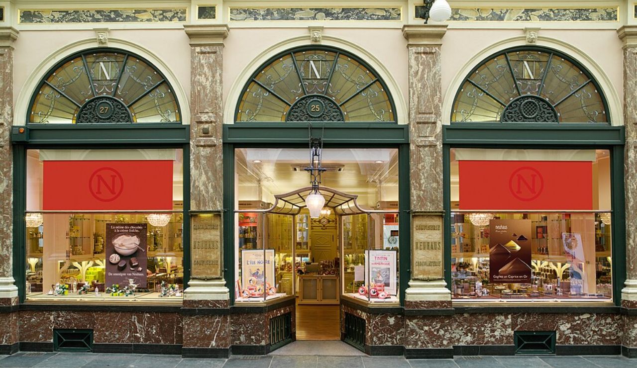 Elegant storefront of a Belgian chocolate shop in Brussels, with arched windows, marble columns, and displays of luxury chocolates inside.