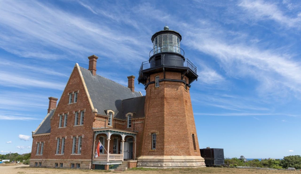 Historic brick lighthouse with attached keeper’s house under a bright blue sky with wispy clouds.