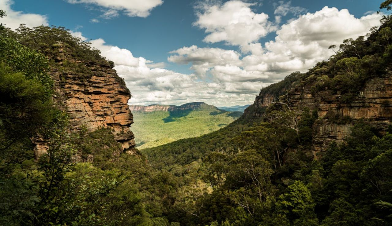 Scenic mountain valley surrounded by steep cliffs and dense forest under a partly cloudy sky.