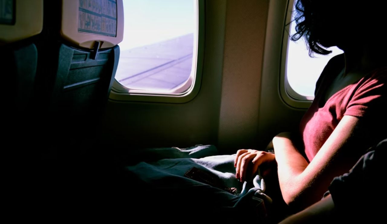 Woman sitting by the airplane window, resting quietly with sunlight casting shadows inside the cabin.