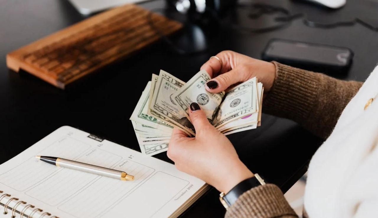 Person counting dollar bills at a desk with planner, highlighting lifestyle budgeting.