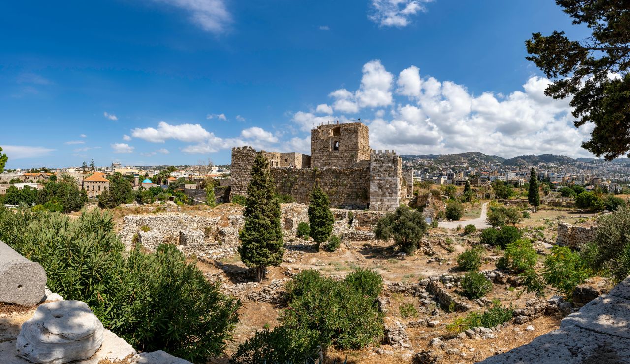 Ancient stone ruins and a medieval castle in Byblos, Lebanon, surrounded by greenery and a cityscape in the background.