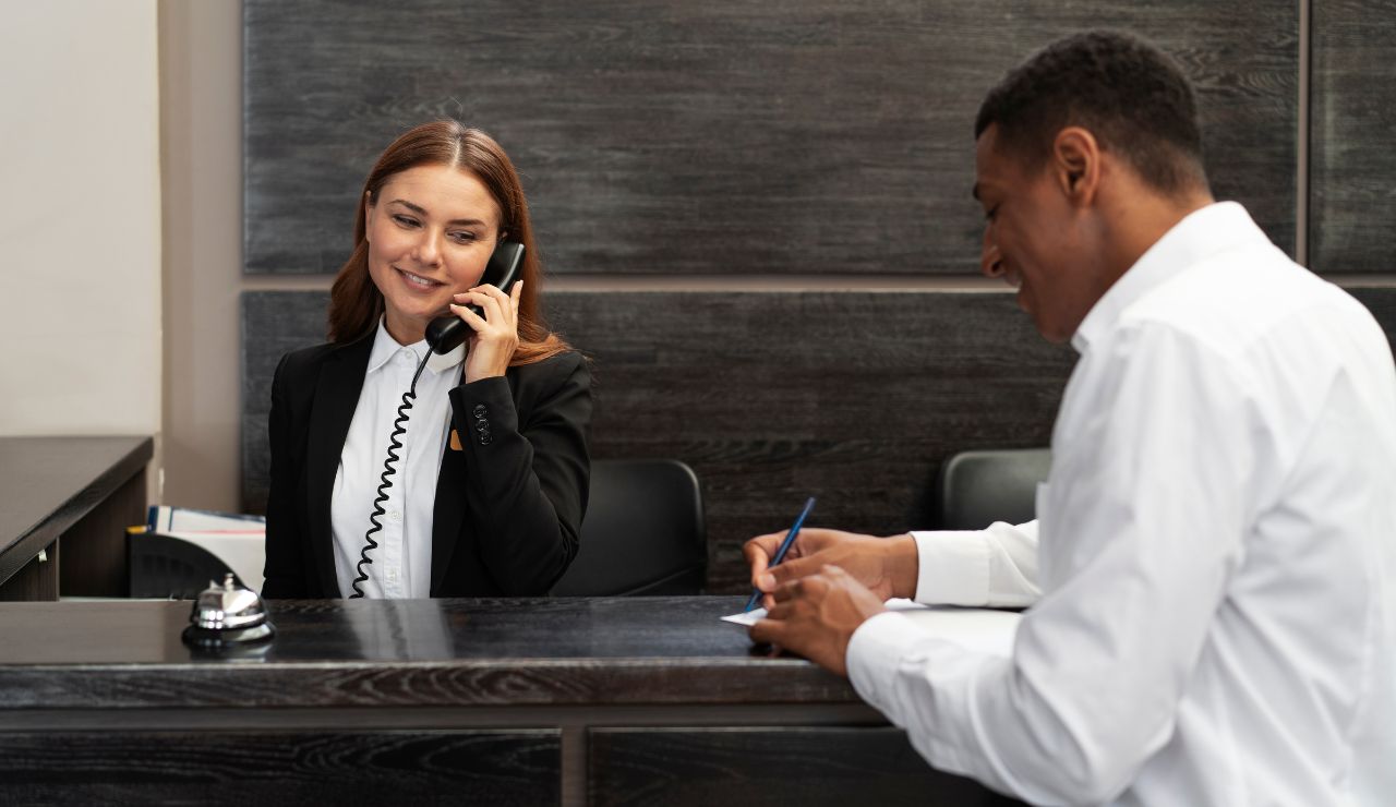 Someone on the phone in a hotel lobby, speaking with a front desk agent.