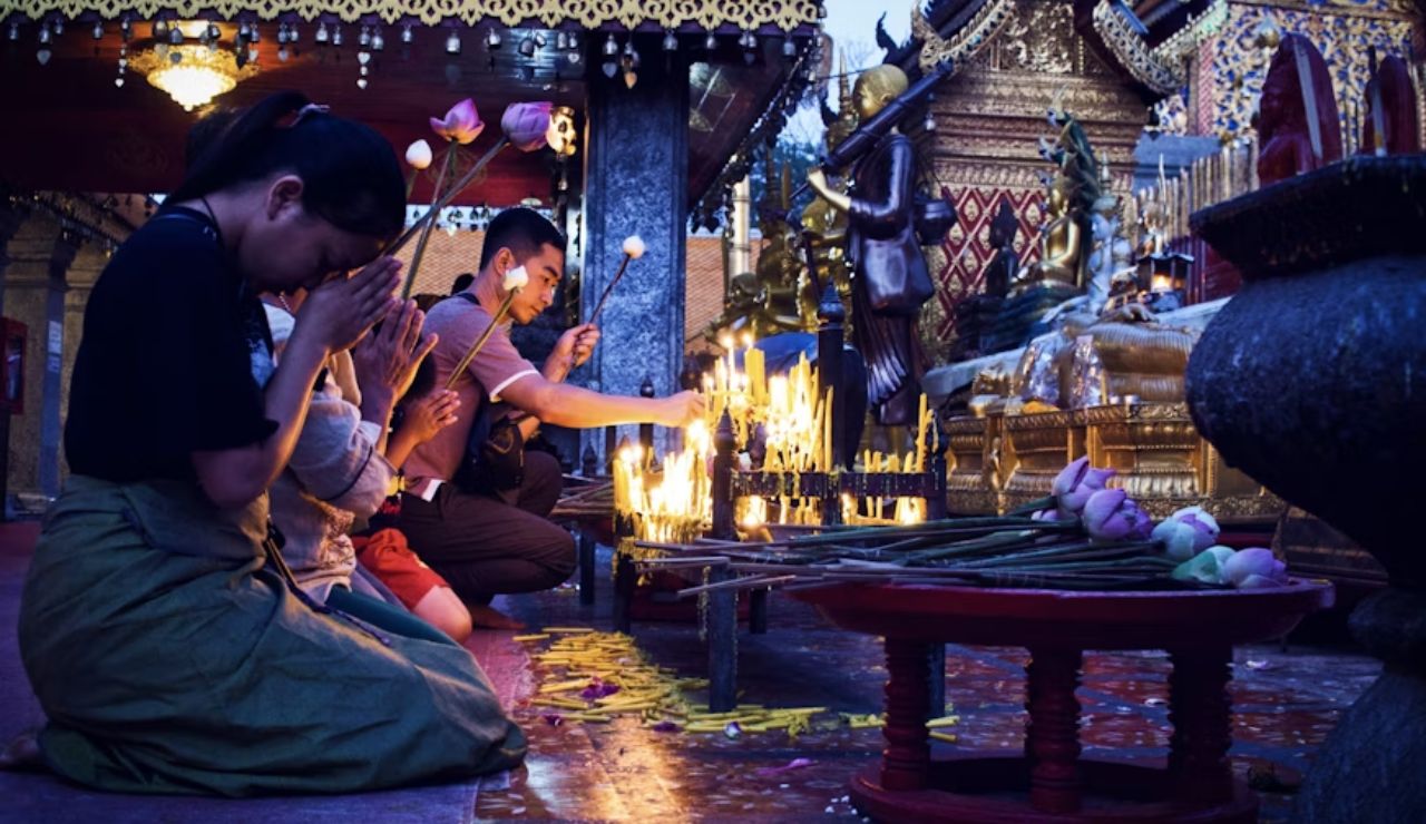 People praying and lighting candles at a Thai temple, symbolizing campaigns promoting cultural respect.