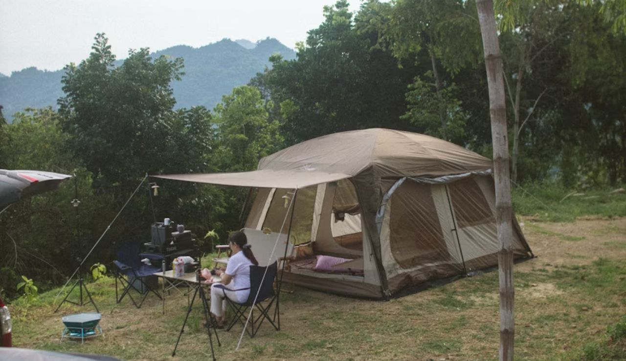 Woman sitting at campsite near large tent, showing growing campground expenses.