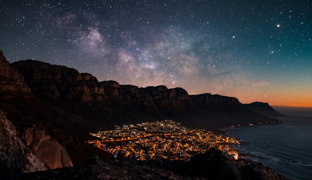 Night view of Camps Bay Beach in South Africa, with city lights glowing beneath the Twelve Apostles mountain range and a star-filled sky above.