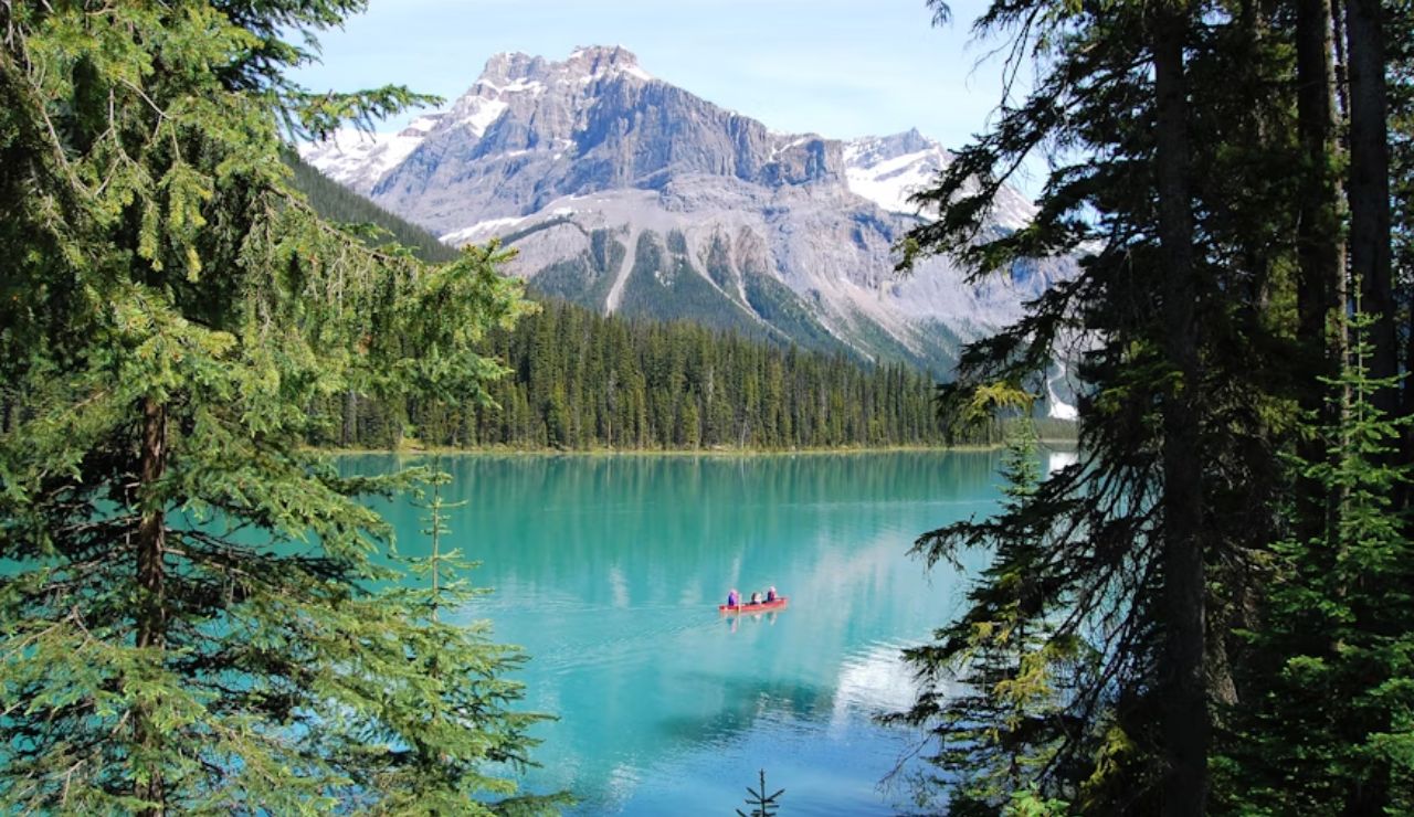 Scenic view of a turquoise lake surrounded by pine trees and mountains, with two people canoeing peacefully in the center.