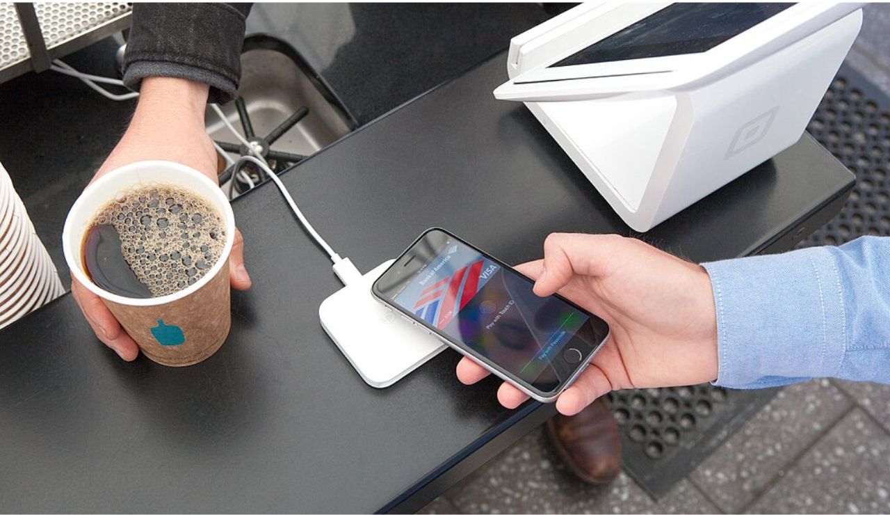 Person using a smartphone to make a contactless payment for coffee at a modern point-of-sale terminal.