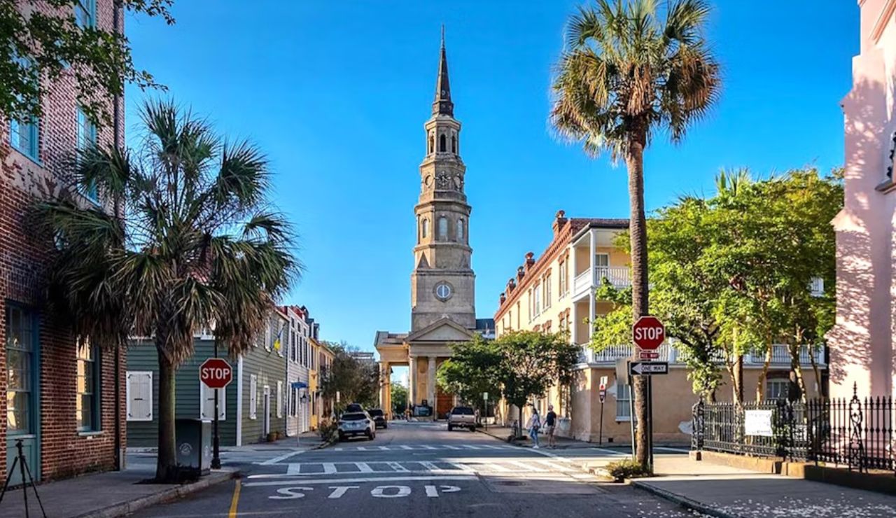 Historic street in Charleston, South Carolina, with palm trees and a view of St. Philip’s Church tower under a clear blue sky.