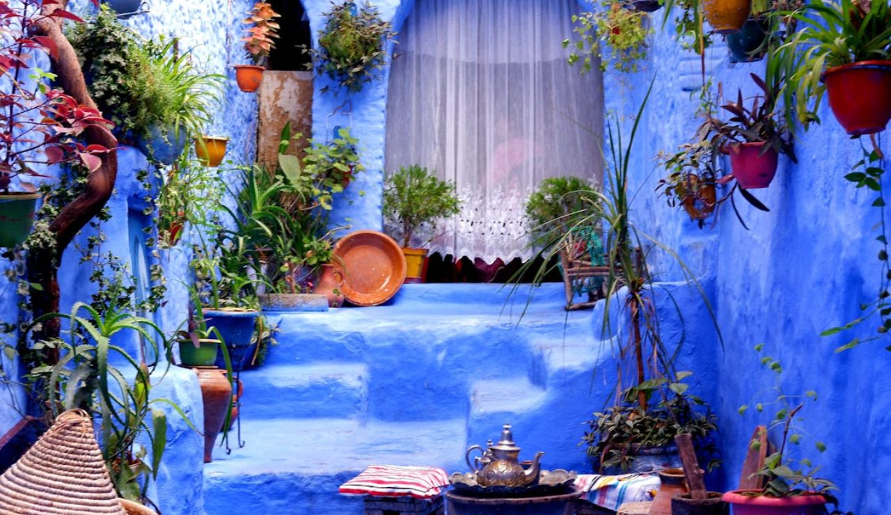 Vibrant blue courtyard in Chefchaouen, Morocco with potted plants, traditional decor, and a tea set on a low table.