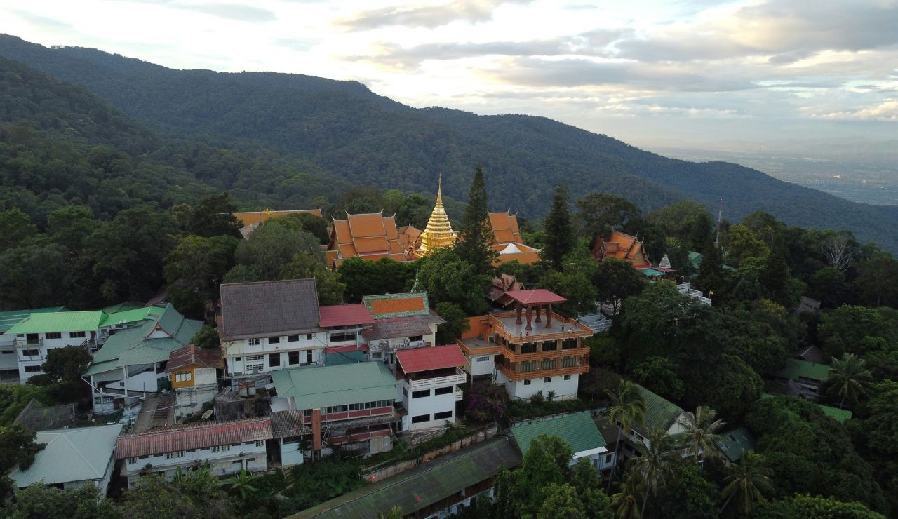 Aerial view of a temple complex with golden spire nestled in a lush, forested mountain area surrounded by traditional buildings.
