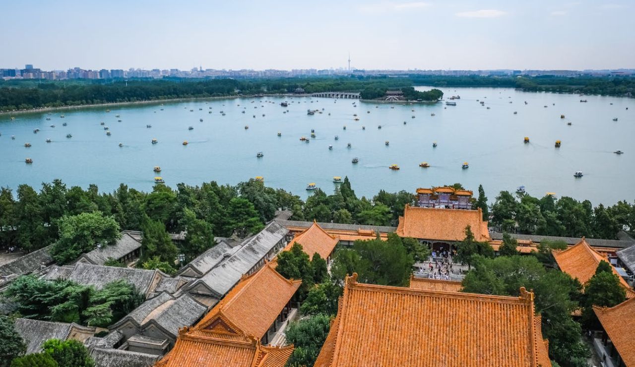 Aerial view of traditional Chinese architecture with orange rooftops overlooking a large lake filled with boats.
