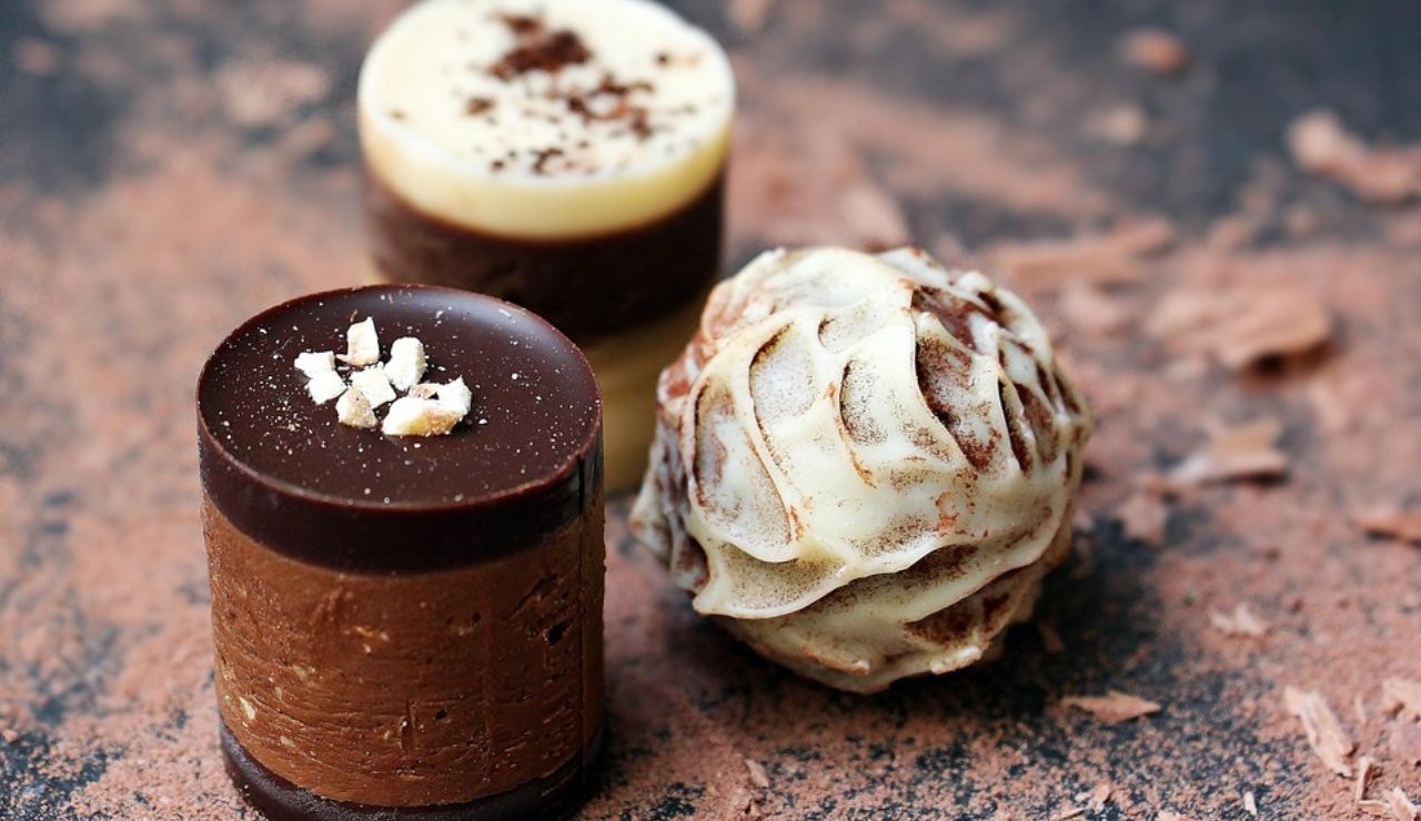 Close-up of artistic Belgian chocolates, including layered pralines and a white chocolate truffle dusted with cocoa powder.