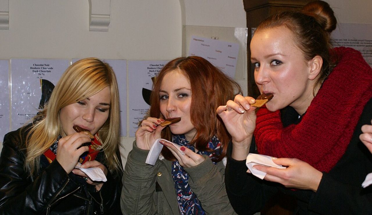 Three women enjoying samples during a chocolate tasting tour, each holding and biting into a piece of Belgian chocolate.