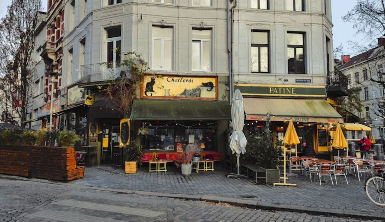Charming street corner in Brussels with two cozy cafés, outdoor seating, and colorful umbrellas on a cobblestone square.