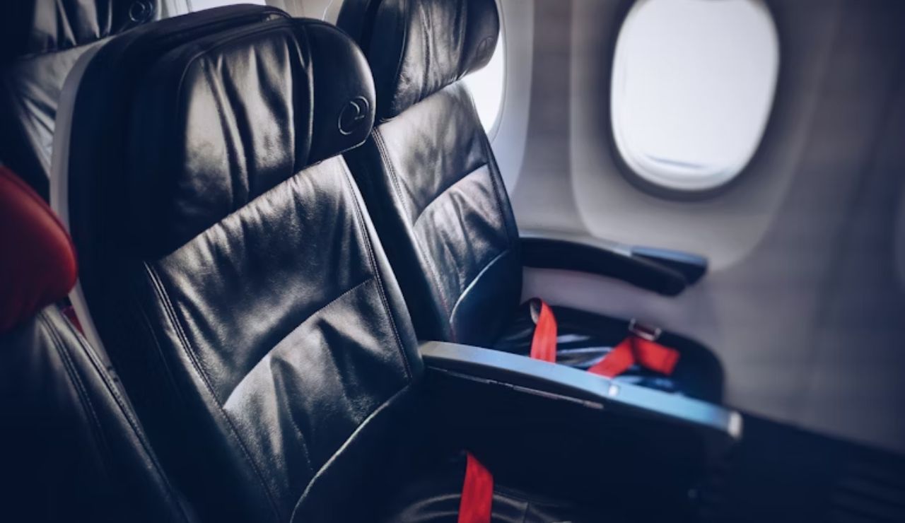 Empty black leather airplane seats with red seatbelts next to a window, inside a commercial aircraft cabin.