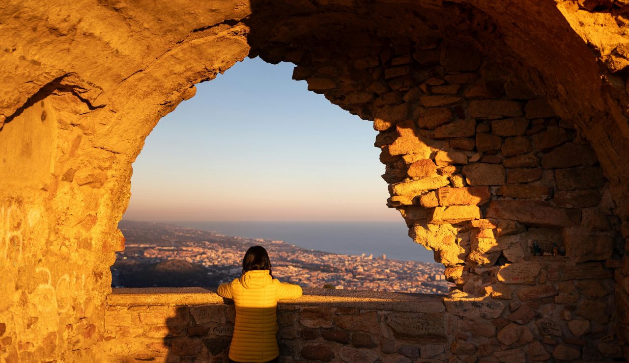 A traveler looking out over a cityscape from a high viewpoint or hill at golden hour.