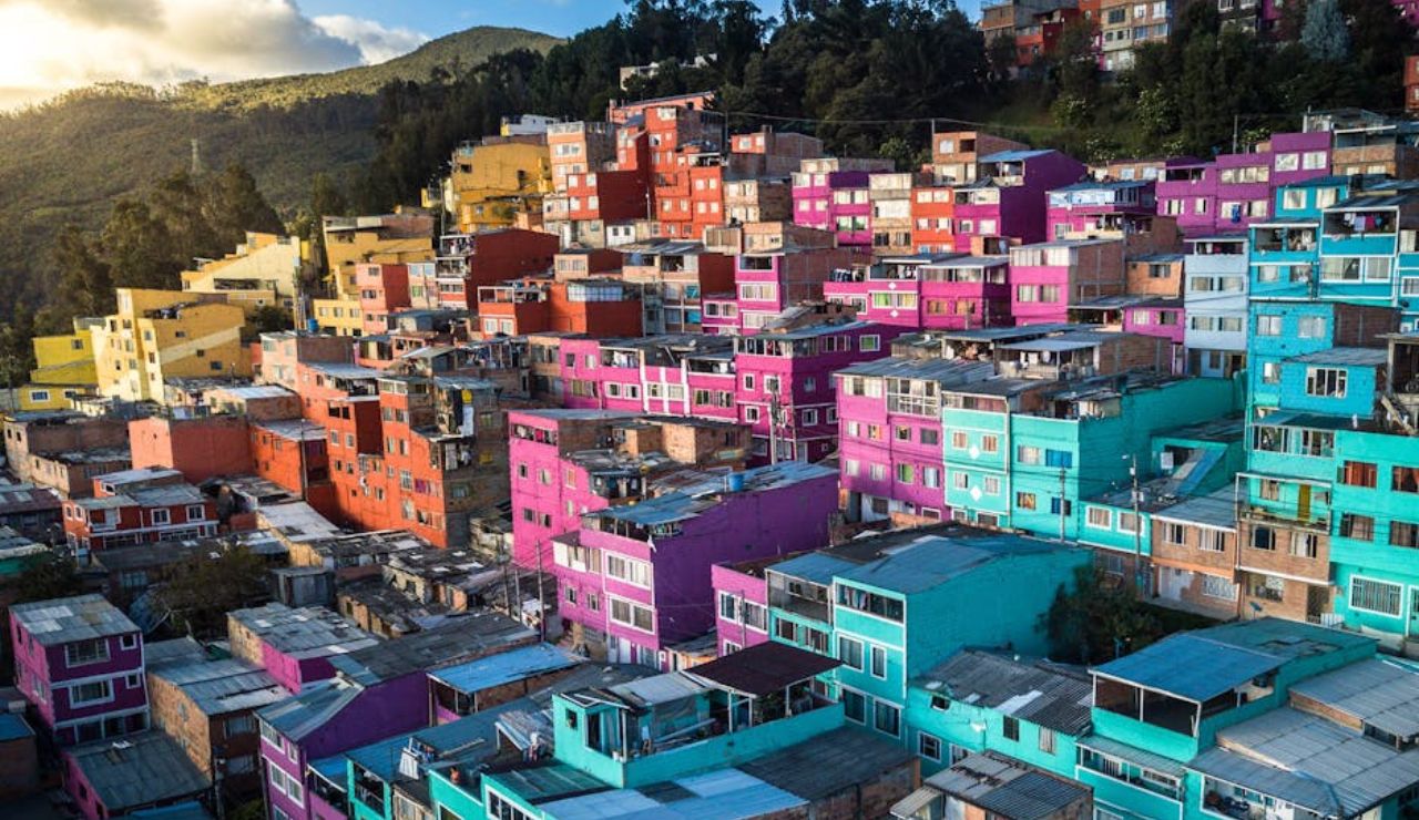 Colorful hillside neighborhood with brightly painted buildings in shades of pink, turquoise, and yellow, set against a mountainous backdrop.