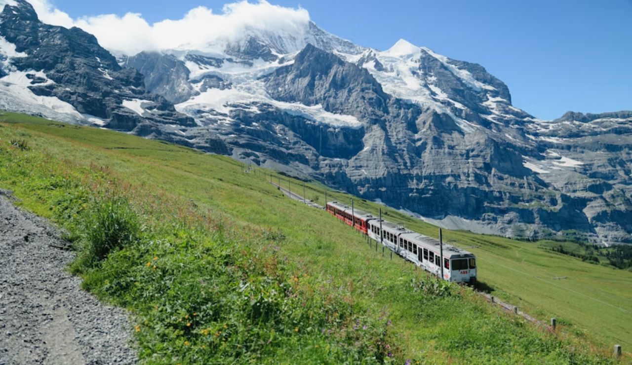 A scenic Swiss mountain landscape with a train traveling through green fields, surrounded by towering snow-capped peaks.
