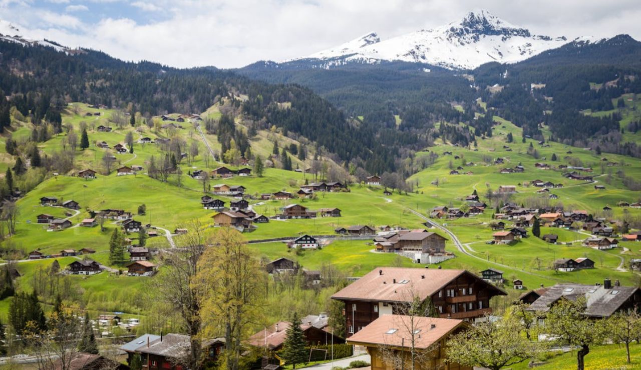 Scenic view of a Swiss village nestled in lush green hills with snow-capped mountains in the backgroound.