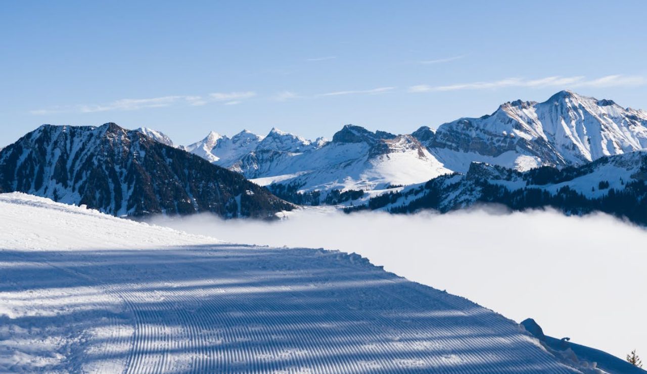 Snow-covered mountains with a clear blue sky and a misty valley below.