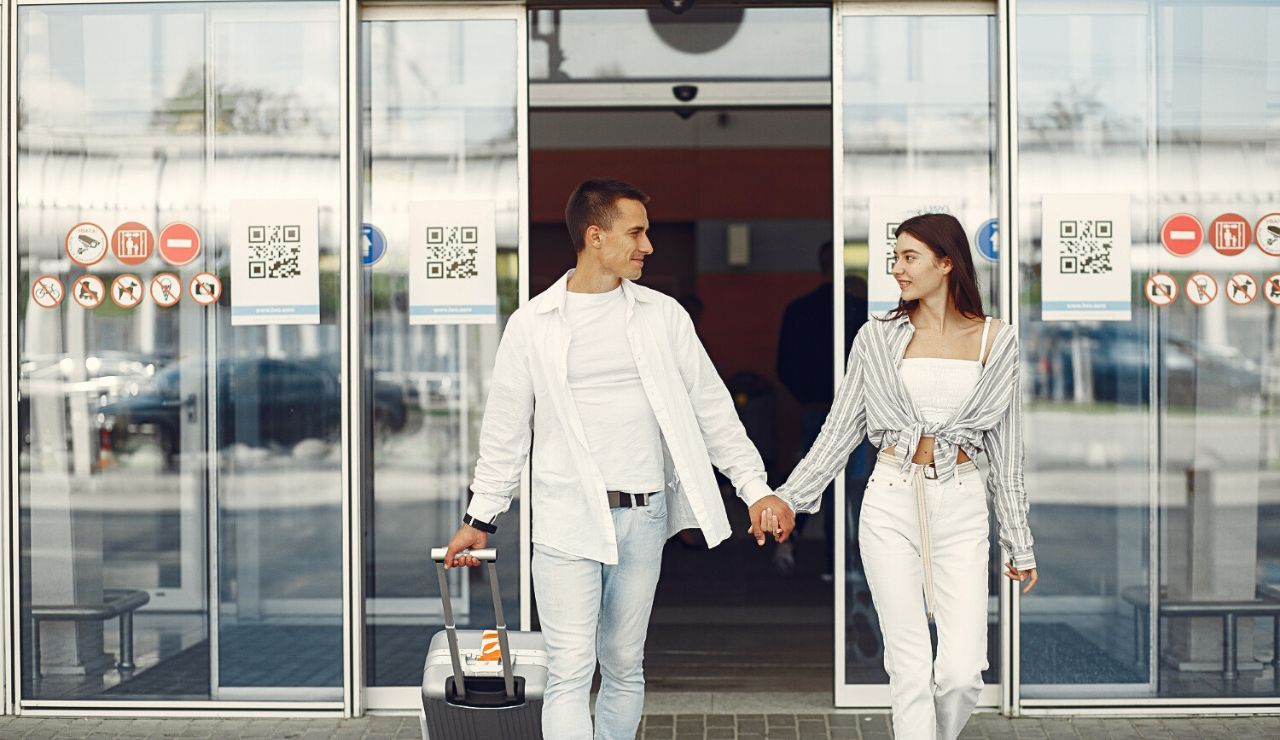 Couple standing at the airport holding a travel bag near the check‑in area.