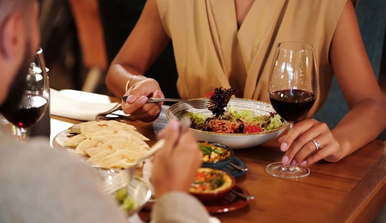Couple dining at a restaurant table with wine, salad, dumplings, and small shared dishes.