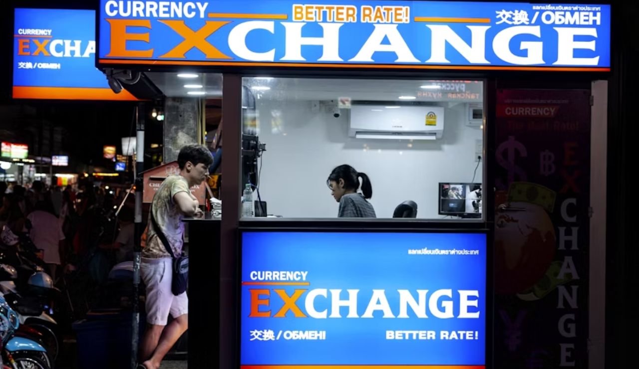 A brightly lit currency exchange booth at night with a customer interacting through the window and a staff member inside.
