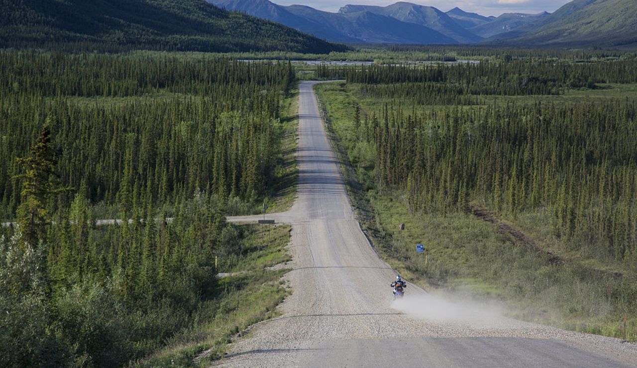 Motorcyclist riding along a gravel stretch of the Dalton Highway through Alaskan wilderness.