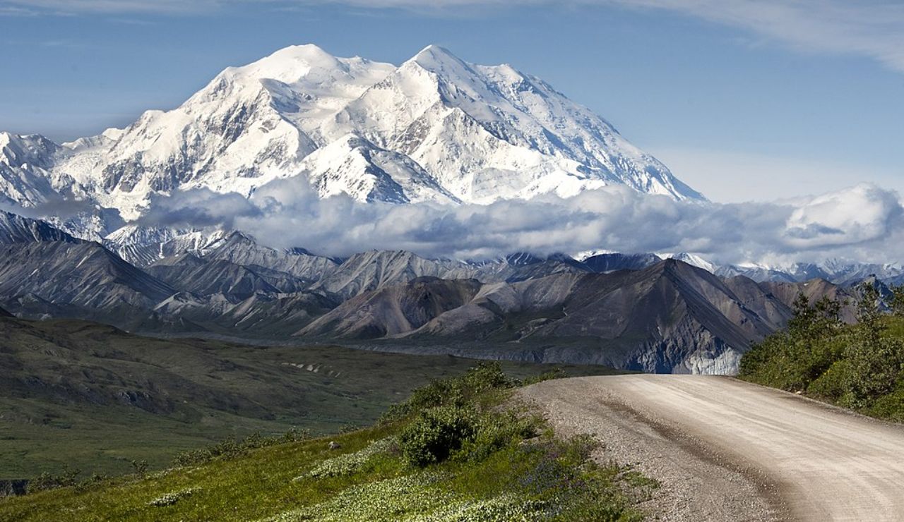 Snow-covered Denali rises majestically over a winding road in Alaska.
