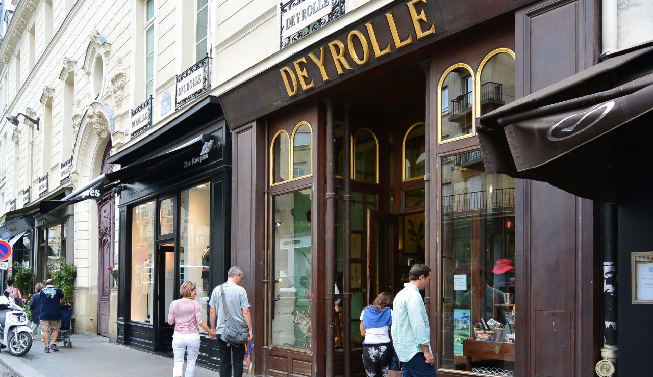 People walk past Deyrolle, a historic Paris shop with large windows and gold lettering.
