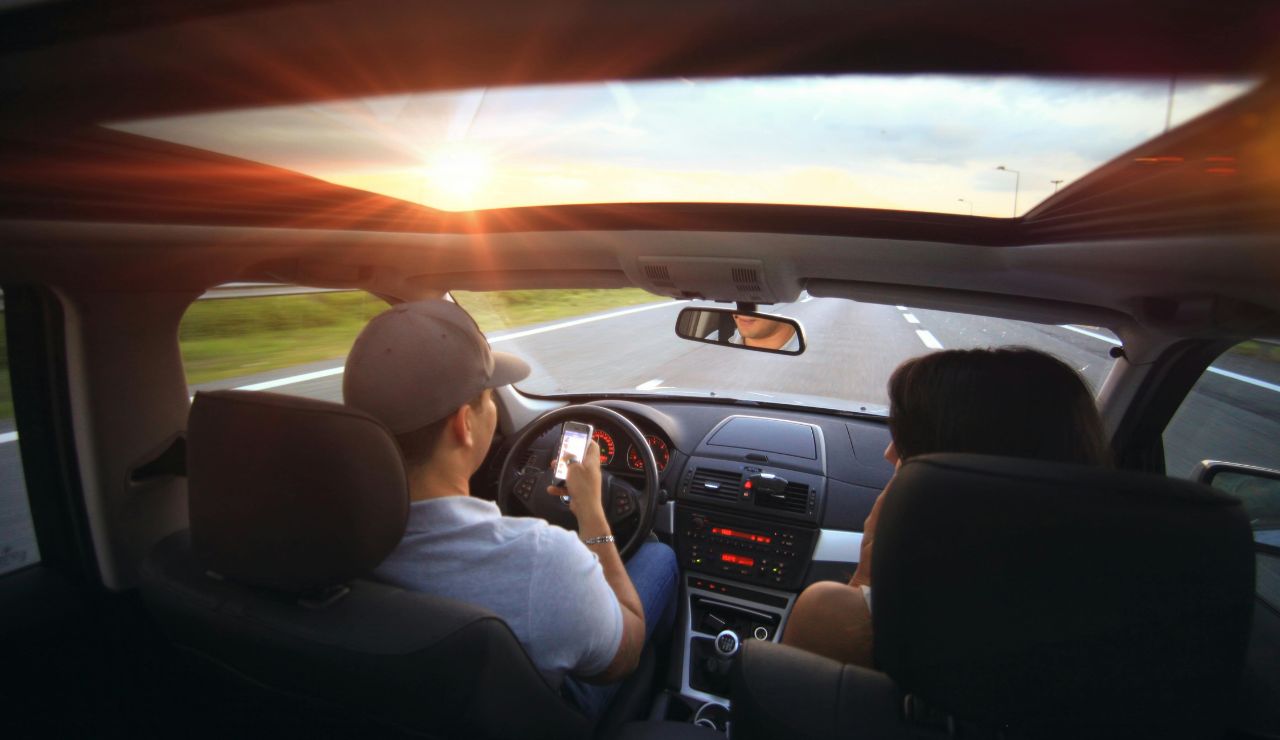 Man using a smartphone while driving on a highway at sunset.