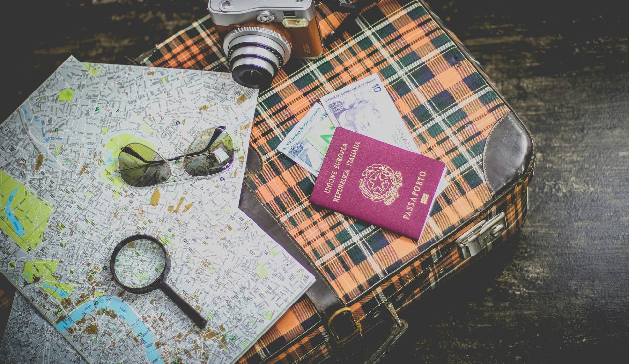 Travel essentials including a map, passport, camera, and money on a plaid suitcase.