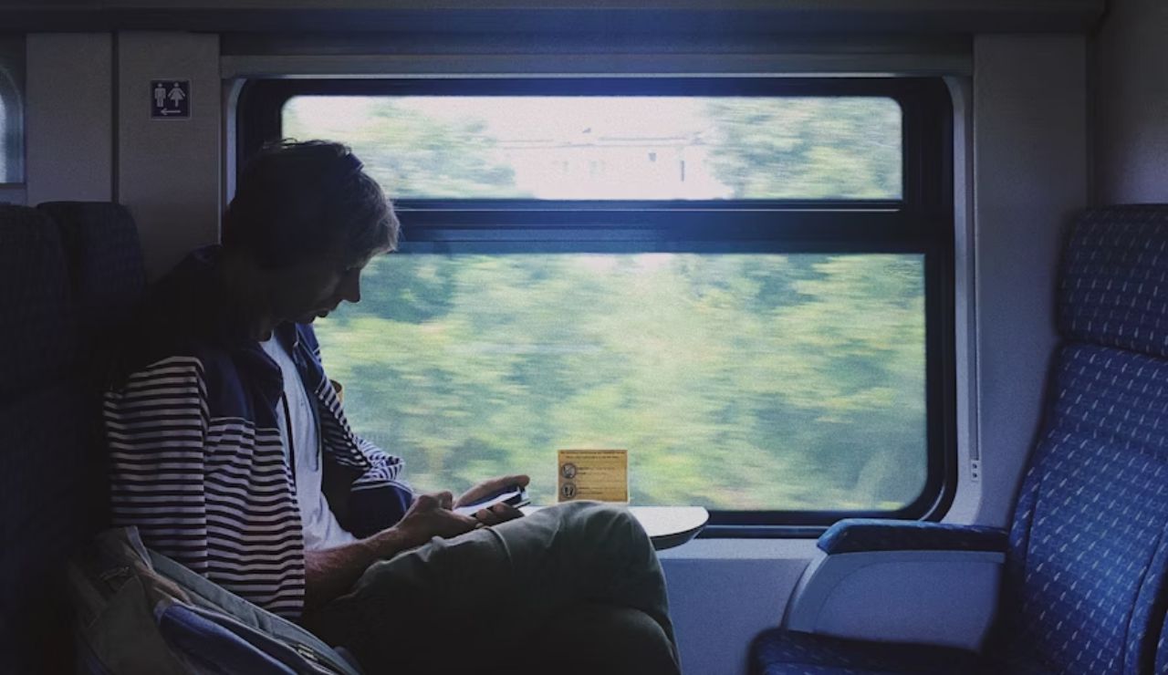 Person sitting alone on a train, using a smartphone while looking out at the blurred green scenery through the window.