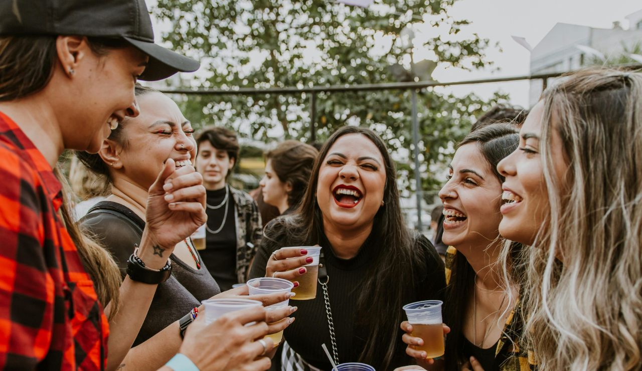 Group of women laughing and holding drinks at an outdoor gathering.
