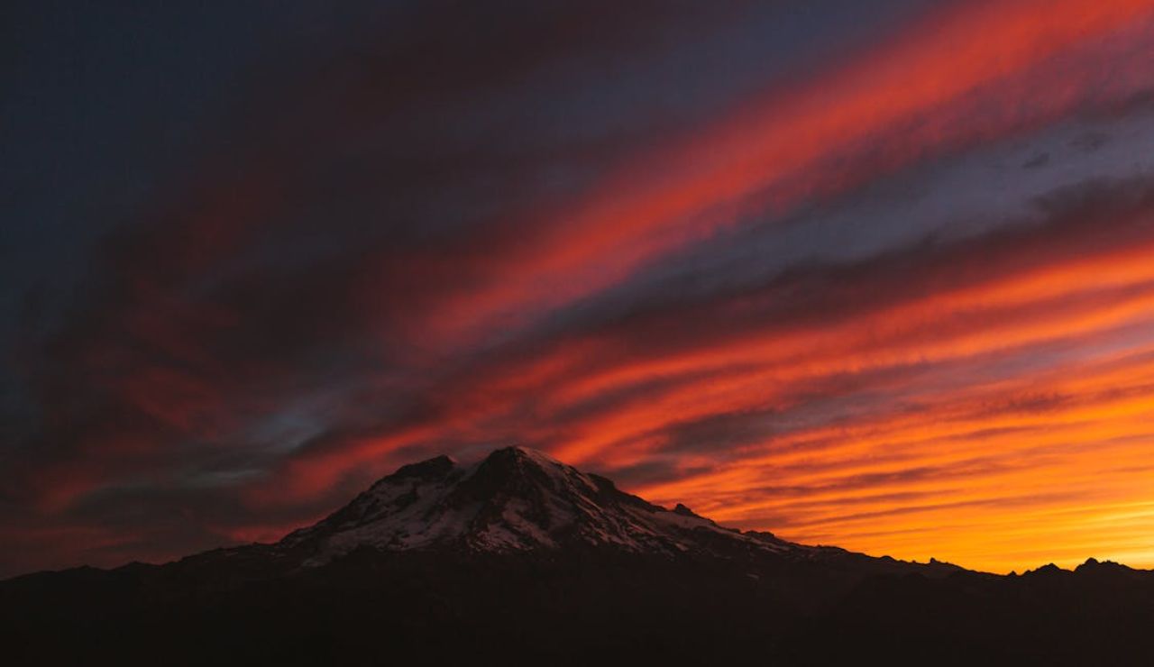 Snow-capped mountain silhouetted at sunset with fiery skies, symbolizing volcanic risks in the Pacific Northwest.