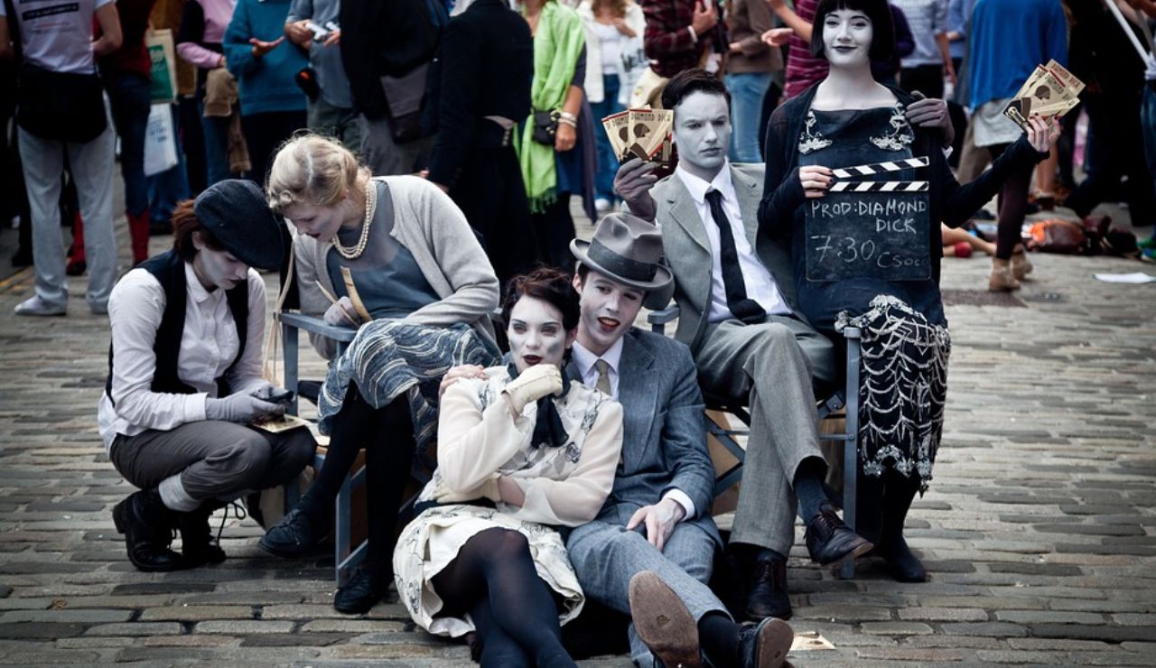 Street performers dressed and painted to resemble vintage black-and-white film characters pose dramatically during a public festival, surrounded by a crowd.