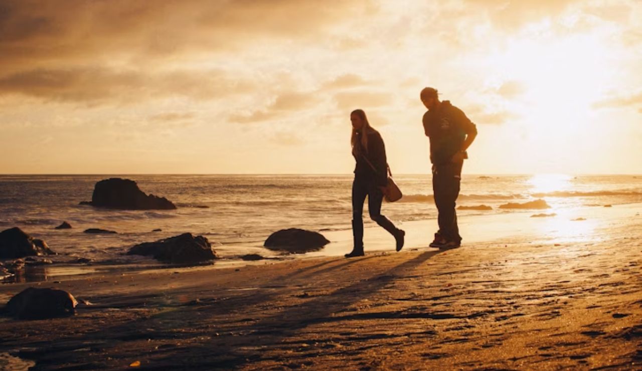 Two people walking along El Matador Beach in California at sunset, with golden light reflecting on the sand and rocks.