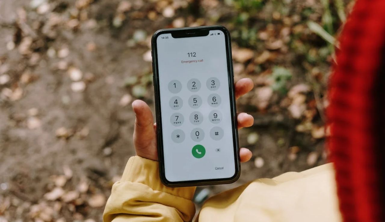 A person holding a smartphone with the emergency number 112 dialed on the screen, standing outdoors in a forested area.