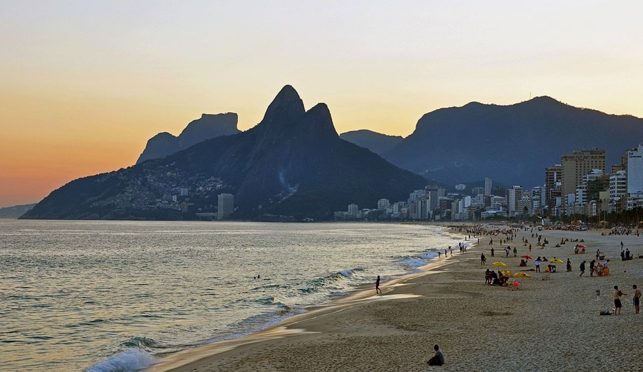 Sunset view of Rio de Janeiro's iconic beach with towering mountains in the background and people enjoying the shore.