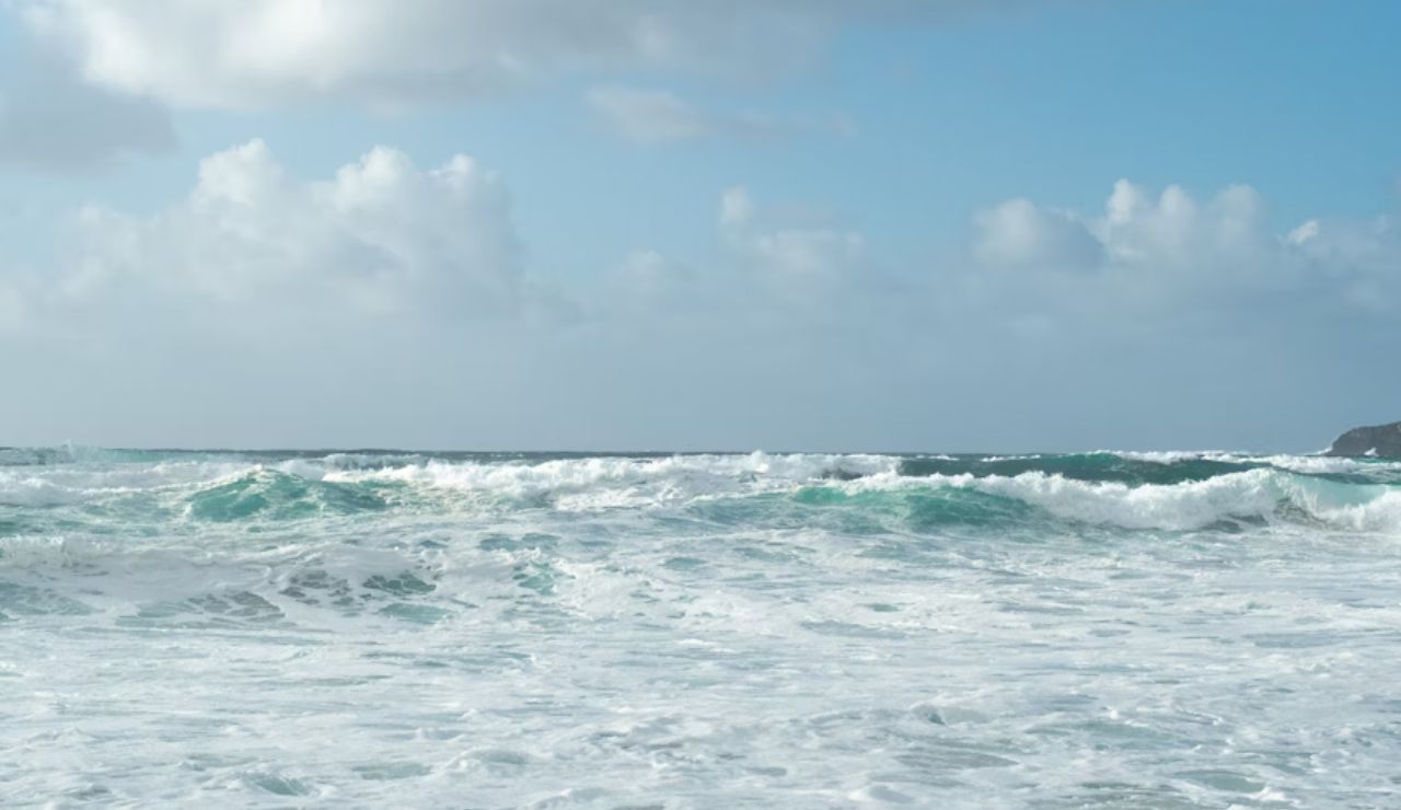 Rough ocean waves crashing under a partly cloudy blue sky.