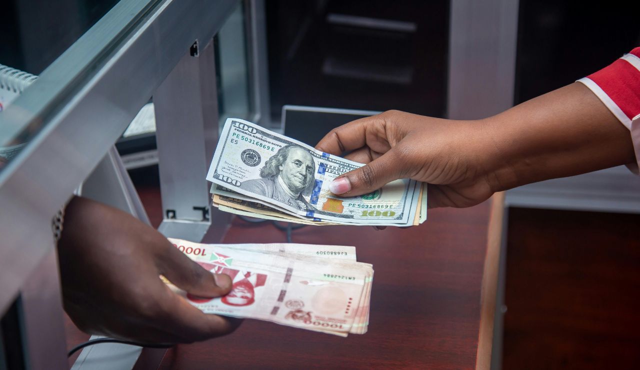 Hands exchanging US dollars and Nigerian naira at a currency counter.