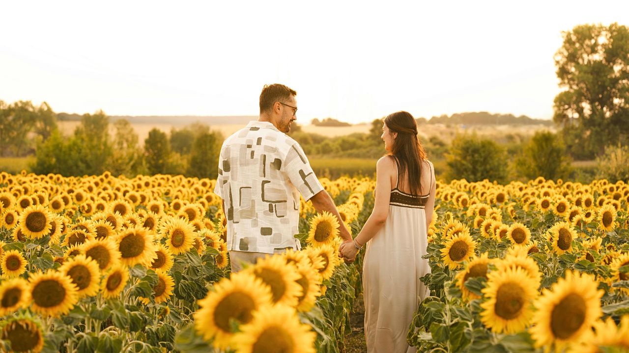 A couple walking hand-in-hand in a field with warm light and local charm.