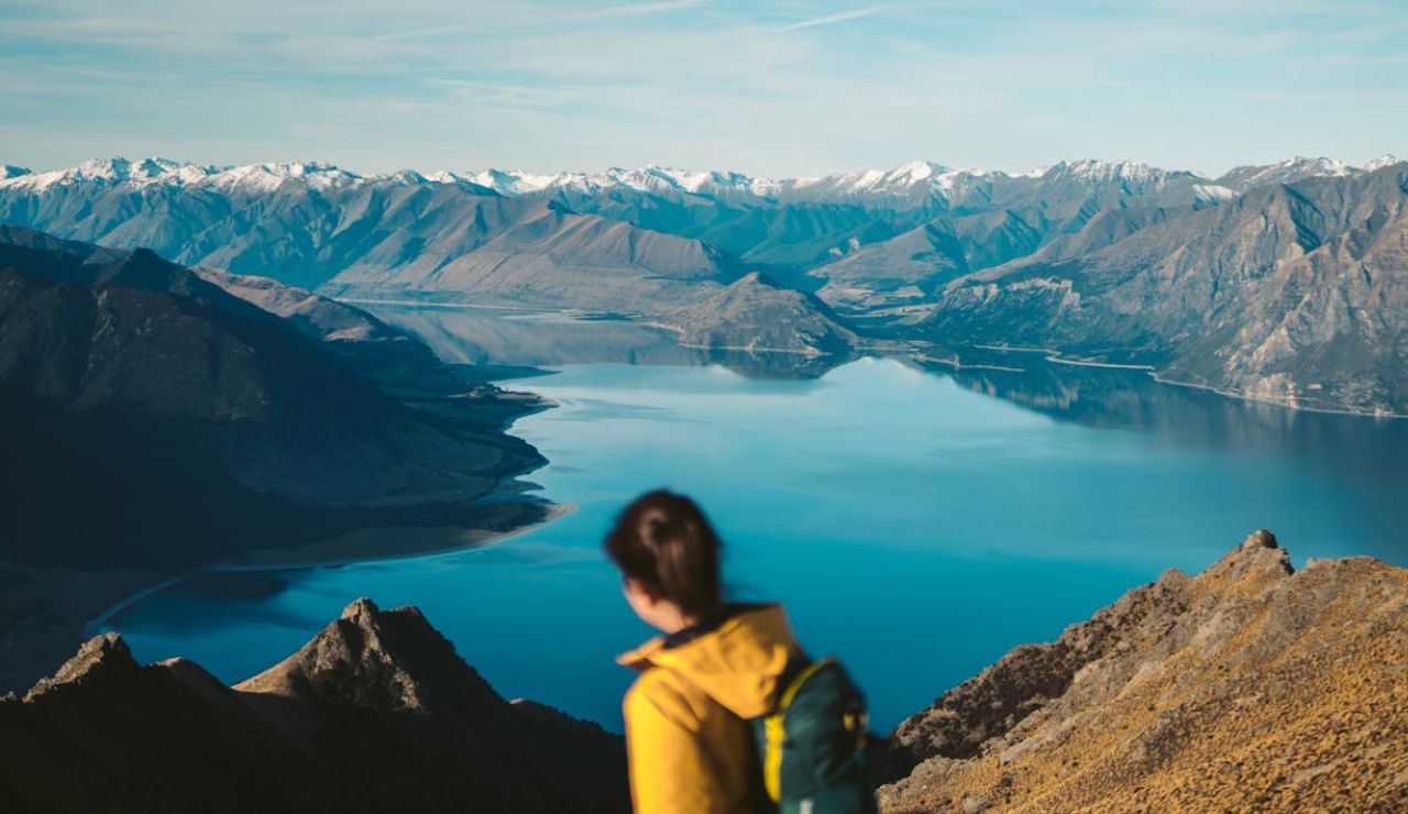 Hiker admiring a stunning mountain lake view with snow-capped peaks in the distance.