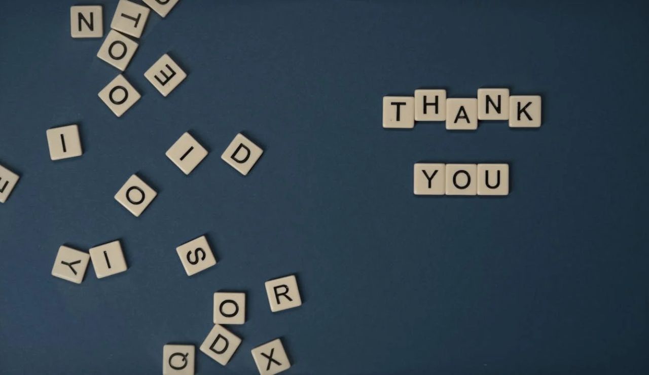 Scrabble tiles scattered on a surface, with "THANK YOU" neatly arranged on the right.