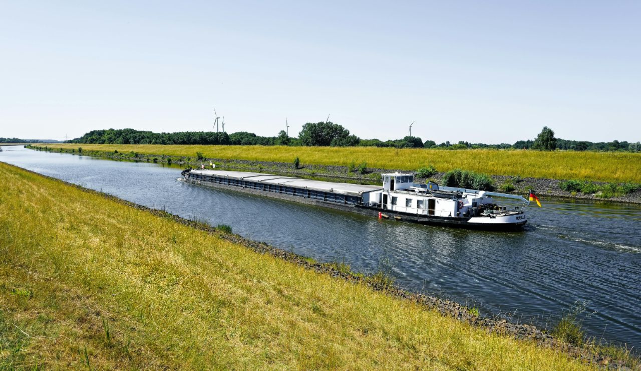 A small barge cruising along a canal in the French countryside with vineyards nearby.